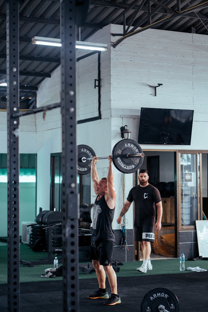 services-02 A man lifting a barbell in a modern gym with gym equipment in the background.