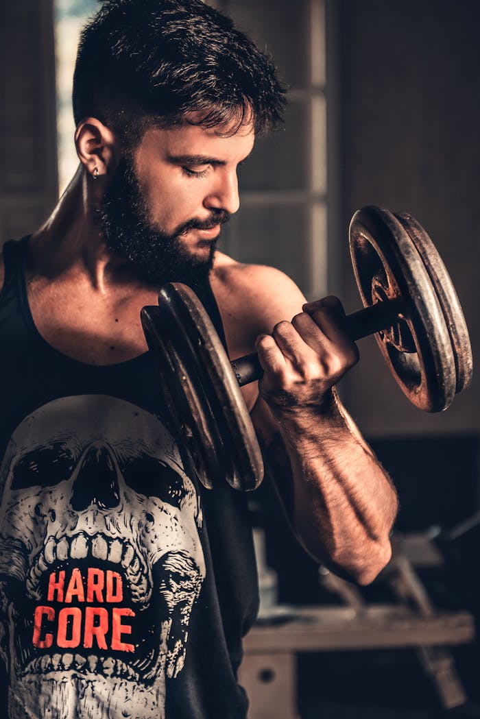 services-04 Bearded man in gym lifting a heavy dumbbell, showcasing strength and fitness.