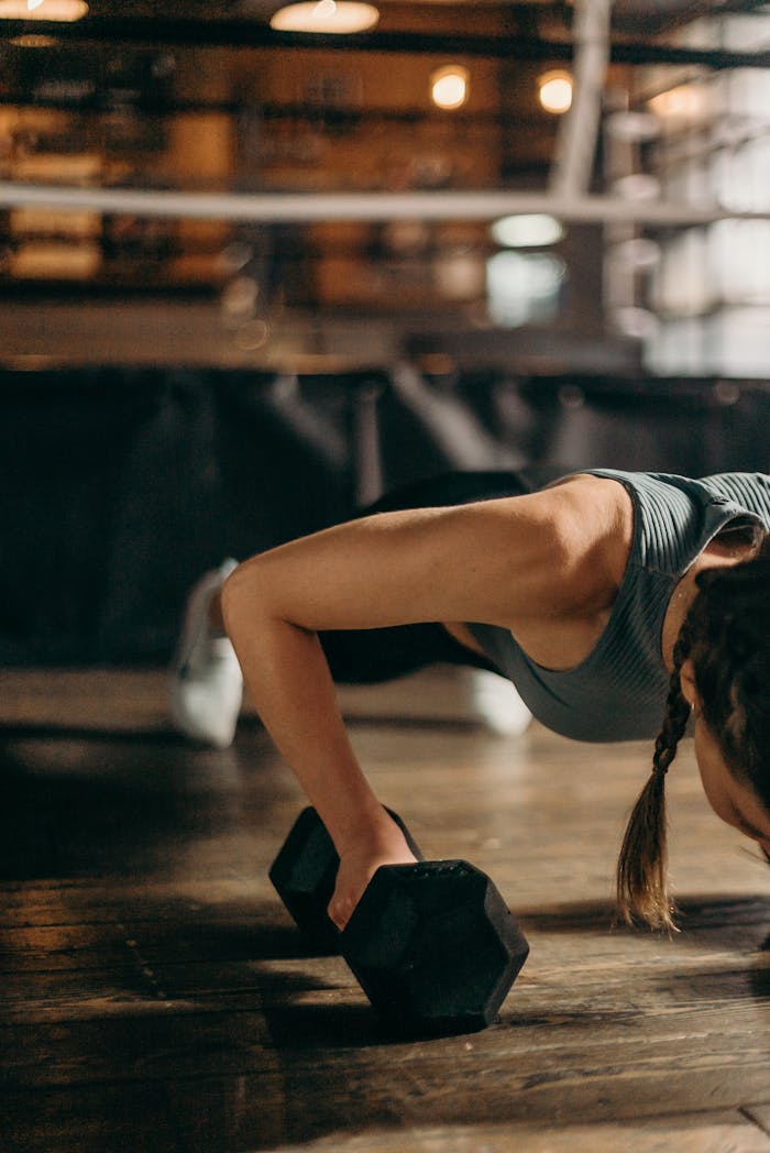 services-01 Fit woman doing a dumbbell push-up in a gym, highlighting strength and fitness training.